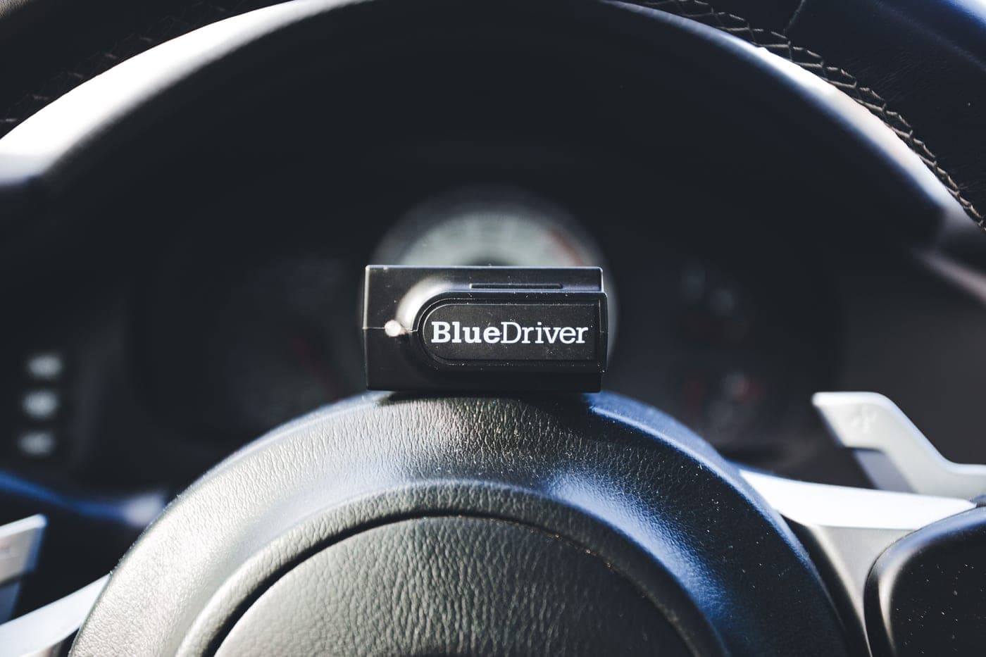 A code reader placed on a car's steering wheel, showing automotive diagnostic tools