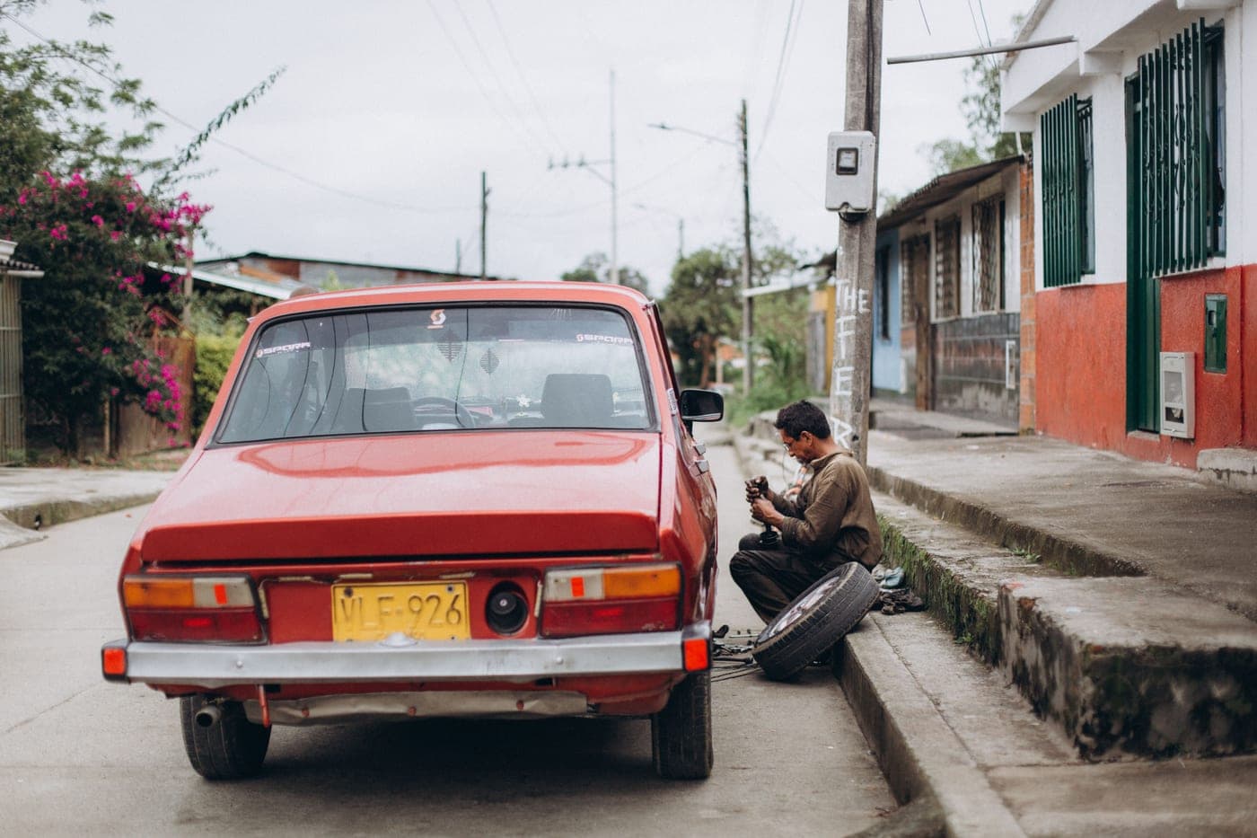 A mechanic repairing a red car at the side of a street