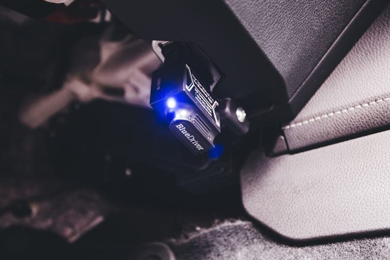 A Bluetooth code reader plugged in inside a vehicle, lit by a blue indicator