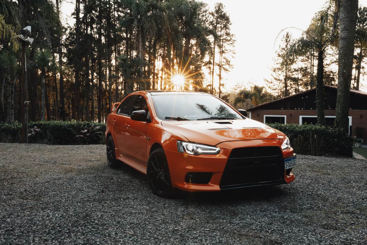 An orange sports car parked on gravel with a rural background at sunset