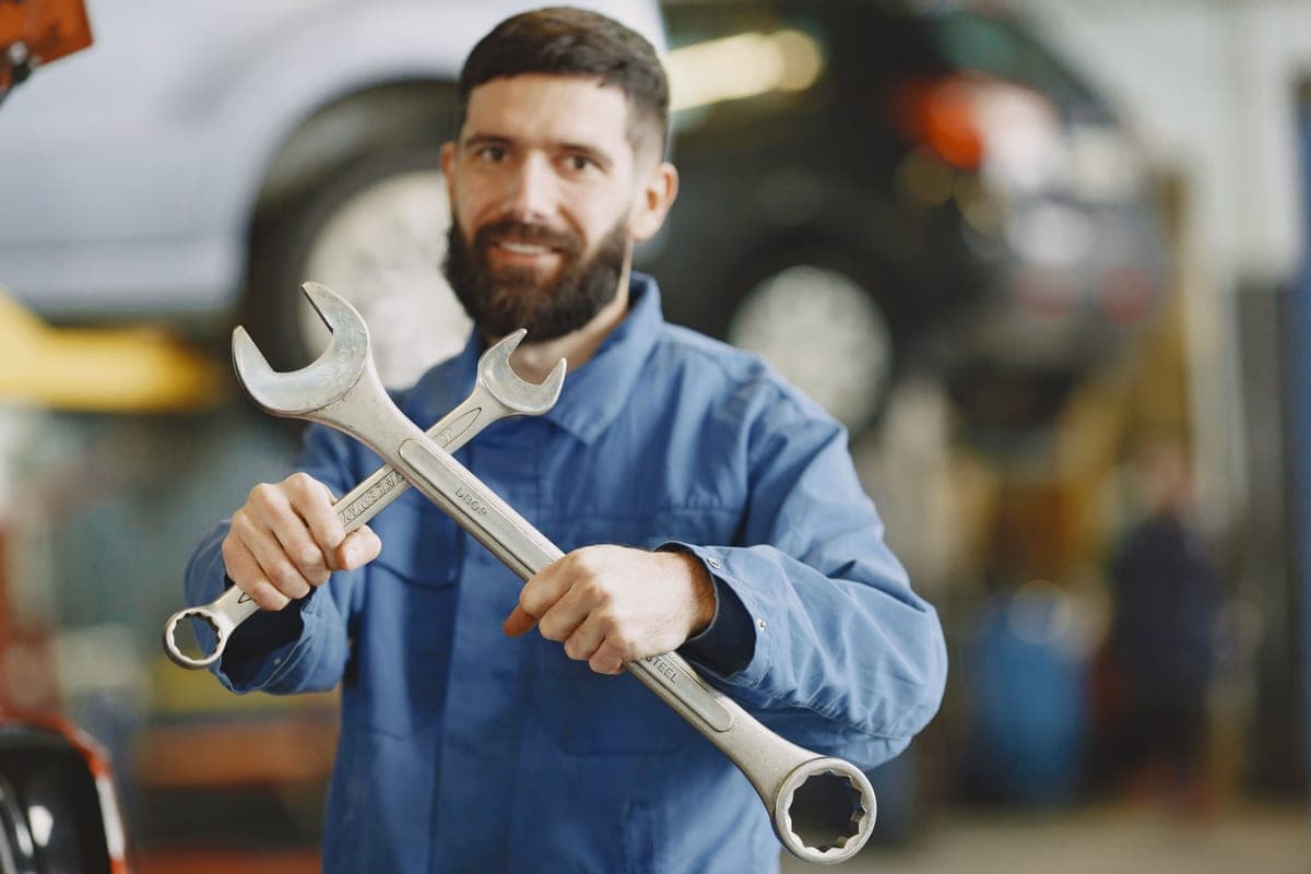 A mechanic in a blue uniform holding wrenches inside an auto repair shop