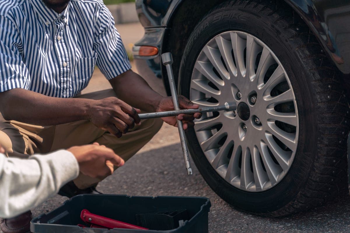 An adult showing a teenager how to change a tire at the roadside